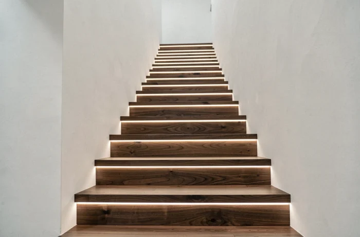Escalier moderne avec bandeaux LED encastrés le long de chaque marche, créant un éclairage rasant et rythmé en bande lumineuse chaude sur les contremarches.