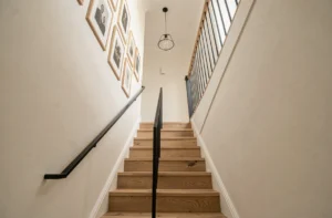 Vue d'ensemble d'une cage d'escalier moderne dans une maison rénovée, avec marches en chêne, rampe en métal noir et décoration murale soignée.