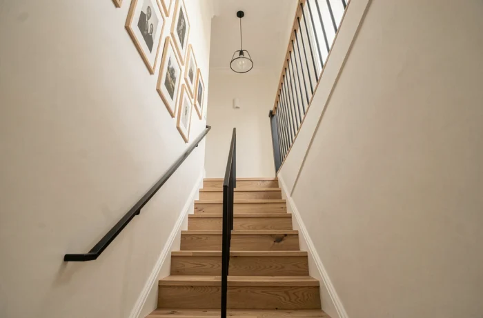 Vue d'ensemble d'une cage d'escalier moderne dans une maison rénovée, avec marches en chêne, rampe en métal noir et décoration murale soignée.
