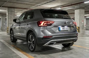 Caméra de recul intégrée dans le hayon d'une Volkswagen T-Roc dans un parking souterrain urbain, vue arrière trois quarts, design 2026